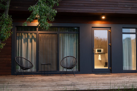 Modern wooden house exterior with two chairs and warm evening lights on the terrace.の写真素材