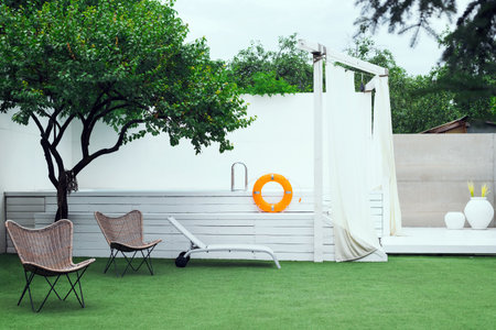 A minimalist outdoor lounge area with a swimming pool, a sun lounger, and two stylish chairs on a...