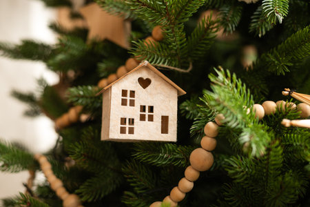 A charming wooden miniature house ornament hangs on a Christmas treeの写真素材