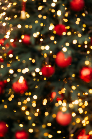 Blurred bokeh background of a Christmas tree with glowing golden lights and round red holiday ornaments.の写真素材