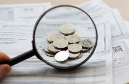 Kyiv, Ukraine. March 15, 2026. Magnifying glass over coins on utility bills, concept of household...