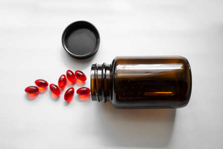 Jars of red pills. Tablets poured out of the jar on white background. Glass brown pill bottleの写真素材