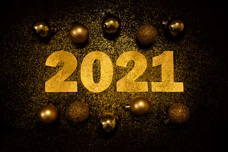 Gold numbers 2021 on black background. Scattered gold sparkles and Christmas balls. Happy New Year