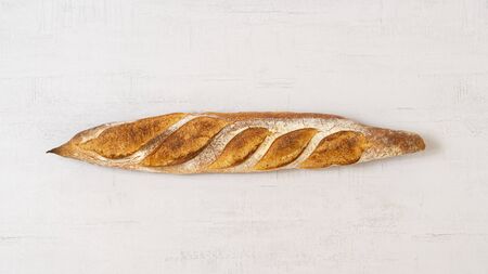 Fresh whole baguette in the centre on a grey background.