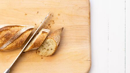 Cut French baguettes, bread with a knife on a wooden cutting board. Close up. On a left side. Copy...