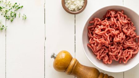 Raw meat farce in a bowl. There is a little brown bowl with salt and pepper mill, green herbs near...