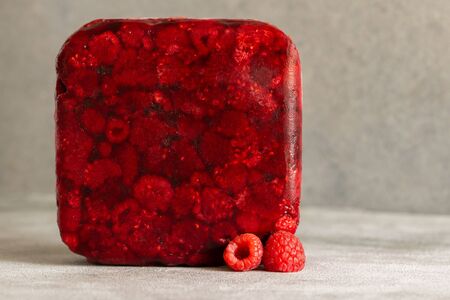 Red frozen raspberry cube near fresh raspberry. Creative photo. Copy space. Grey background.の写真素材