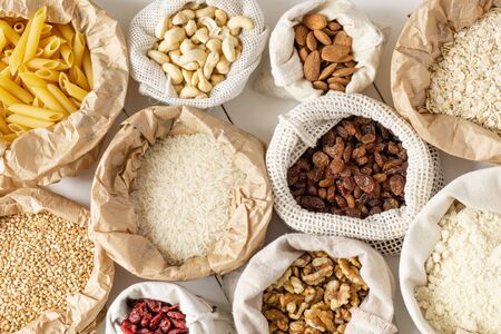Groats, pasta, nuts, and dried fruits in paper and cotton bags on white wooden table. Top view. Zero waste, eco friendly or plastic free lifestyle concept.の写真素材