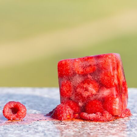 Red frozen raspberry cube near fresh raspberry. Creative photo. Copy space. の写真素材