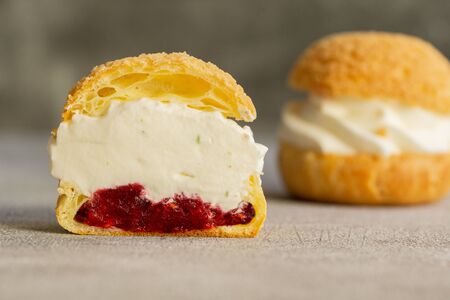 Choux pastry cookies filled with whipped cream and raspberry jelly on gray background. Concept: bakery, french dessert. Selective focus.の写真素材