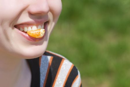 Smiling mouth with piece of mandarin orange   