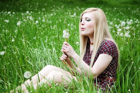 blonde blowing at dandelion in green grass  の写真素材