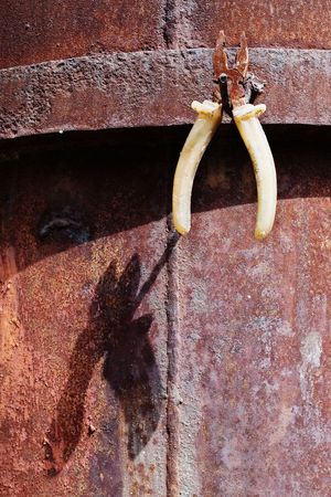 Old rusty pliers hanging on hook against corroded metal sheet