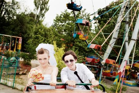 Bride and groom riding rollercoaster in amusement park with blurred ferris wheel in the backgroundの写真素材
