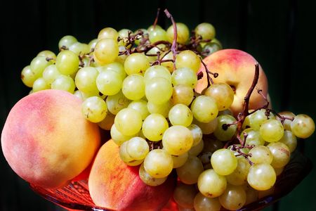Fruit piece with bowl of fresh grapes and peaches against dark background with selective focus