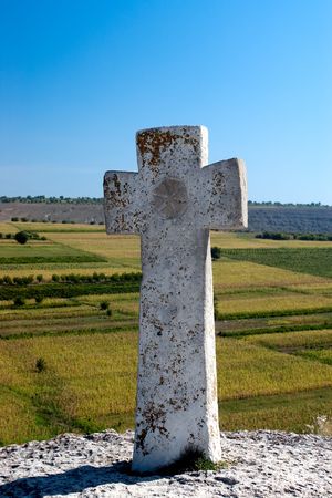 Ancient Christian stone cross on the hill with blurred fields in the background and blue sky, Old Orhei place in Moldovaの写真素材