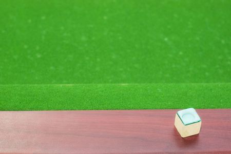 Piece of cue chalk on wooden rail with out of focus green baize
