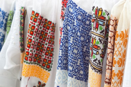 Row of white textile shirts with colored ethnic folk patterns and selective focusの写真素材