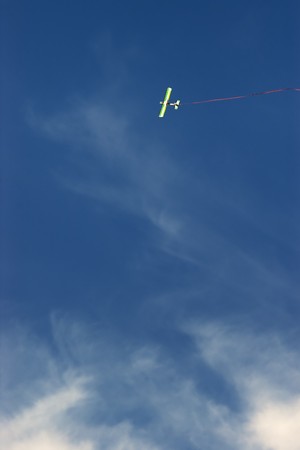 Radio controlled toy airplane with red ribbon against blue sky with white cloudsの写真素材