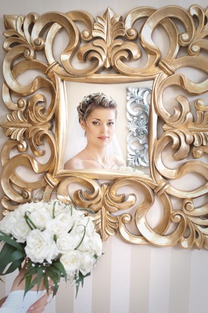 bride with bouquet of flowers looking at herself in the antique mirror with golden flower patternsの写真素材