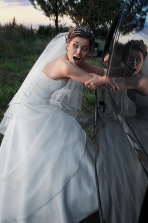 Scared bride in white dress being kidnapped into a black car in the eveningの写真素材