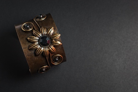 Bronze bracelet with flower and black stone against dark background with copy spaceの写真素材