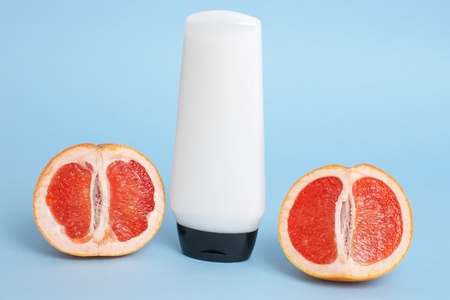 white cosmetics container with two halves of cut red grapefruit on blue background の写真素材