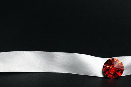 White ribbon with red precious stone on dark black textured background with copy spaceの写真素材