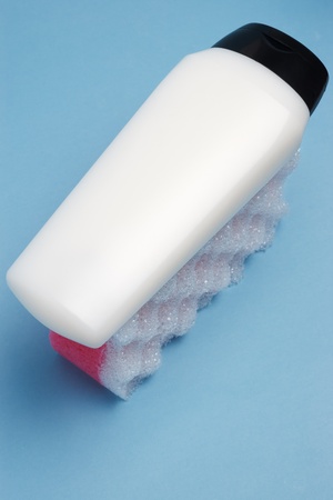 White blank cosmetics bottle on red and white porous bath sponge on side against blue paper background with selective focusの写真素材
