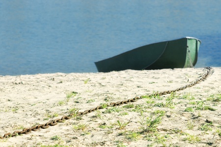 Long rusty chain on sand beach with blurred boat and blue waterの写真素材
