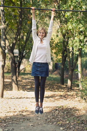 Young cheerful woman smiling and hanging by the bar in a park with selective focus