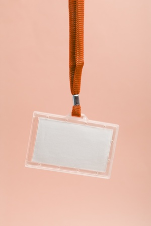 Hanging blank business plastic badge with orange neck strap against rosy background の写真素材