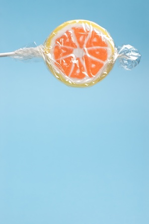Closeup of wrapped orange lollipop on a stick against blue background with copy spaceの写真素材