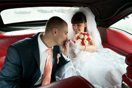 Groom kissing hand of bride with bouquet of flowers inside red car with selective focusの写真素材
