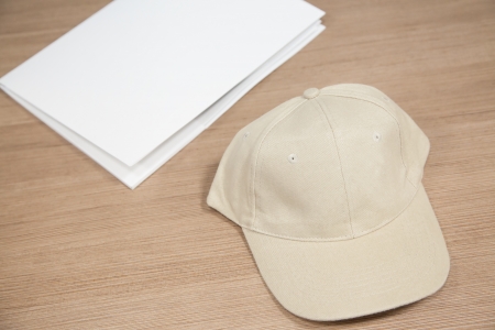 Brown empty baseball cap without logos and white folder on wooden table with selective focusの写真素材