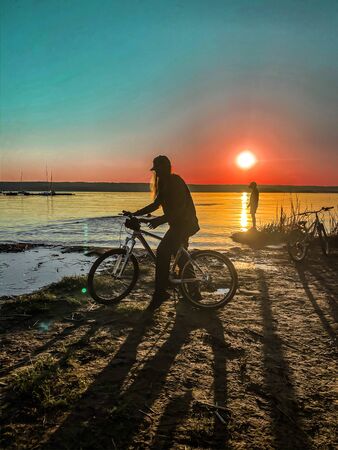 silhouette of a young girl at sunset on the background of the river with bike, summer and sports ,art processingの写真素材