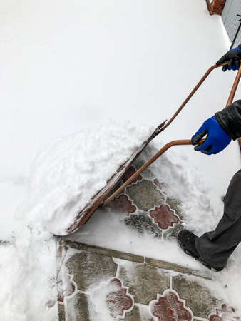 man cleans snow in the winter in his yard near the houseの写真素材