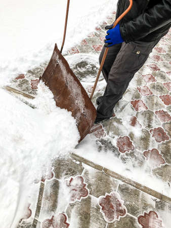 man cleans snow in the winter in his yard near the house