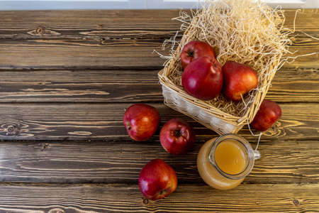 Red apples in a basket and apple juice in a jug on a wooden tableの写真素材