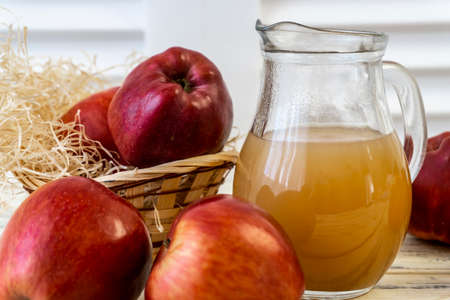 Red apples in a basket and apple juice in a jug on a wooden tableの写真素材