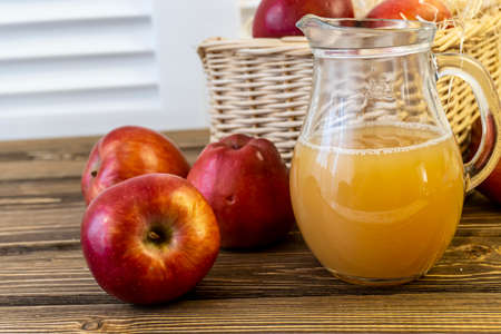 Red apples in a basket and apple juice in a jug on a wooden tableの写真素材
