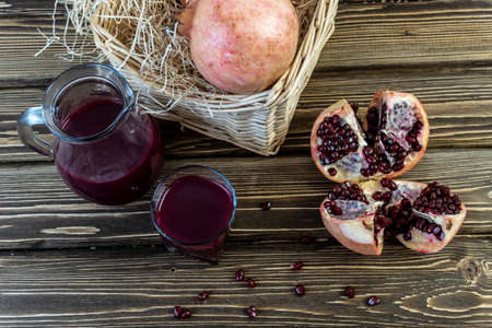 Pomegranates in a basket and on the table on a wooden background. Pomegranate juice in a jug and...