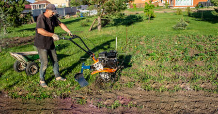 Male in the spring plows the earth in working clothes with a motoblock, walk-behind tractorの写真素材