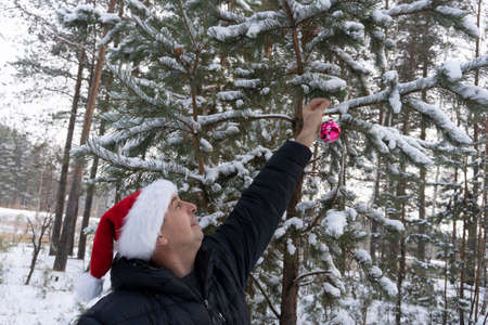 a man in a santa hat with a christmas ball in the winter in the forestの写真素材