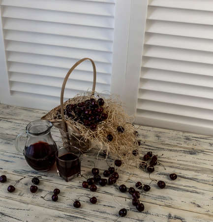 Cherry and cherry juice or wine on a wooden table, a decanter and a glass with juice, a basket with cherriesの写真素材