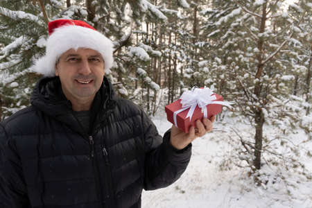 a man in a santa hat with a christmas present in the winter in the forestの写真素材