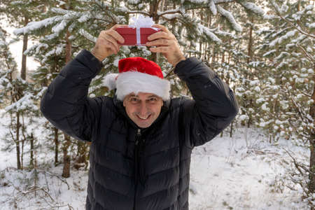 a man in a santa hat with a christmas present in the winter in the forest