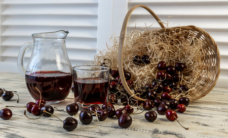 Cherry and cherry juice or wine on a wooden table, a decanter and a glass with juice, a basket with cherriesの写真素材