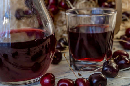 Cherry and cherry juice or wine on a wooden table, a decanter and a glass with juice, a basket with cherriesの写真素材