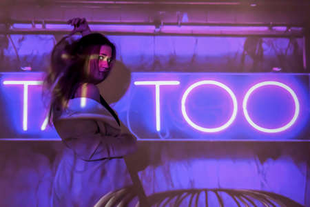 silhouette of a young beautiful woman on the background of neon projector inscriptions, slight blur, tattoo letteringの写真素材